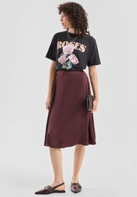 Czarny T-shirt z nadrukiem róży i napisem "ROSES", zestawiony z bordową, zwiewną spódnicą midi oraz ciemnobrązowymi butami wsuwanymi z metalowymi zdobieniami.