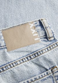 Denim blu chiaro sbiadito con una toppa in pelle, caratterizzato da lettering bianco. Accentuato da cuciture gialle e un classico design a cinque tasche.