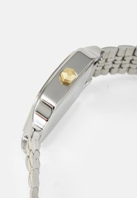 Edelstahlarmbanduhr mit silberner Oberfläche, hexagonaler goldener Krone und Gliederarmband. Rechteckiges Zifferblatt von der Seitenansicht sichtbar.
