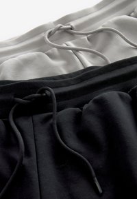 Deux paires de pantalons de survêtement, une gris clair et une noire, chacune avec une taille visible et des cordons noués.