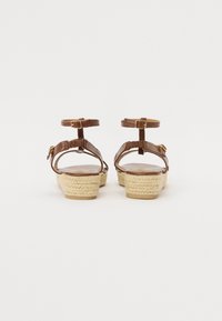 Brown leather heeled sandals with ankle straps, woven jute platform, and smooth insole, featuring gold-tone hardware accents.