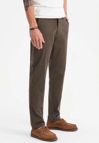 Chinos marron avec une coupe droite, fabriqués à partir d'un tissu texturé. Associés à des chaussures bateau beiges. Présente un design subtil et une silhouette élégante.