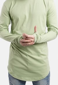 Lange mouw shirt van lichtgroene katoen, met duimgaten in de manchetten, een ronde zoom en een aansluitend ontwerp, gedragen over versleten blauwe jeans.