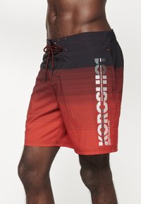 Costumi da bagno da uomo in gradiente dal rosso al nero, con strisce orizzontali e stampa del logo. Realizzati in tessuto leggero con cordino regolabile.