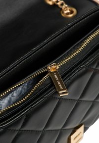 Zwarte gewatteerde handtas met een gouden ritssluiting en een merkpuller. Binnenkant gevoerd met een gestructureerde stof; met een glad, mat lederen buitenkant.