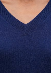 Námořnická modrá svetr s výstřihem do V vyrobený z měkké pletené látky, s žebrovanými manžetami a lemem, s jemnou texturou.