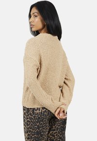 Pull en beige à texture avec une coupe décontractée et des manches longues, associé à un pantalon à imprimé léopard. Le pull a une surface douce et duveteuse.