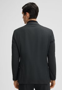 Donkergrijze getailleerde blazer voor heren, gemaakt van een geweven stof, met een enkele split, notch-kleppen en knoopsluitingen op de mouwen. Achteraanzicht alleen.
