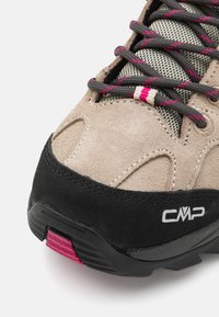 Scarpa da trekking in suede beige con suola in gomma nera, dettagli rosa e lacci grigi. Presenta una tomaia texture e una punta rinforzata.