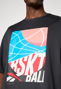 Melnas sporta T-kreklas, kas izceļas ar krāšņu grafisko druku ar basketbola elementiem zilos, rozā un sarkanos toņos. Redzams zīmola logo.