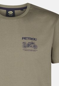 Oliwkowa bawełniana koszulka z okrągłym dekoltem, ozdobiona niebieskim nadrukiem motocykla oraz logotypem marki na lewej klatce piersiowej.