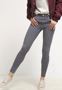 Smala grå jeans i denim med hög midja, fem fickor, knappstängning fram och subtil blekning. Stylar med en vit topp och bomberjacka.