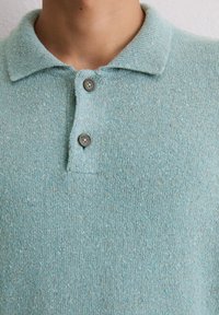 Dzianinowa koszulka polo w jasnoniebieskim kolorze, cechująca się miękką fakturą, dwoma brązowymi guzikami oraz klasycznym kołnierzykiem.