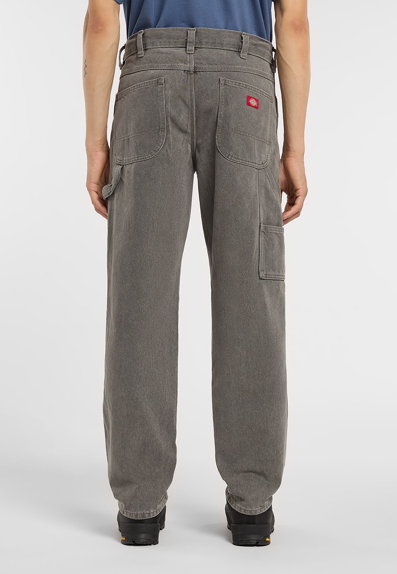 Pantalones cargo gris claro de corte holgado, con múltiples bolsillos y un parche con logo rojo, confeccionados con una tela duradera y acabado texturizado.