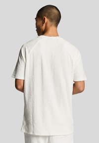 Vit texturerad t-shirt med kort ärm som har ett geometriskt mönster. Mjuk tyg med en något oversized passform och raglanärmar.