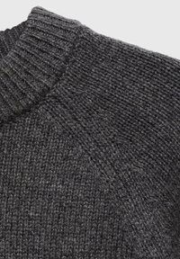 Grauer Strickpullover aus Material mit einem gerippten Kragen und strukturiertem Muster, das ein dickes, kuscheliges Gewebe und subtile Farbvariationen zeigt.
