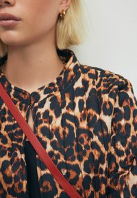 Leopardmønstret jakke i nuancer af orange og sort, med en plisseret design, en krave og en rød skulderrem.