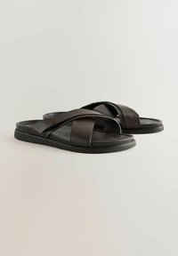 Sandales en cuir noir avec des brides superposées, semelle plate et sans matériel ou embellissements visibles. Texture lisse et design minimaliste.