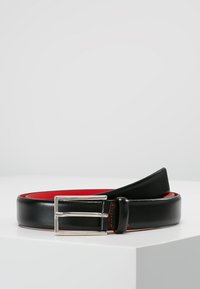 Cinturón de cuero negro con una hebilla rectangular plateada, con forro interior rojo y costuras en contraste. Textura suave y diseño elegante.