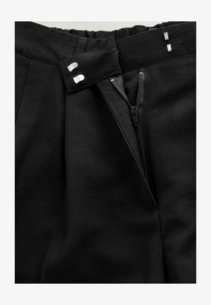 Pantaloni neri caratterizzati da un design plissettato, vita elastica e cerniera laterale con tiralampo in metallo. Texture liscia con una finitura pulita.