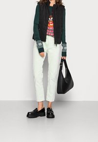 Doudoune noire sans manches portée sur un pull vert avec un motif de renne, associée à un jean vert menthe et des chaussures à plateformes noires, tenant un sac noir.