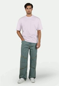 T-shirt de algodão lilás claro combinada com calças de ganga verdes oversized com costuras curvas e pespontos dourados. Ténis brancos completam o visual.