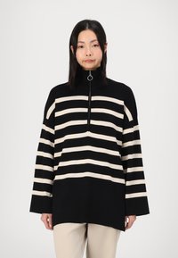 Black and cream striped pullover sweater with a high collar and quarter-zip front. Made of soft fabric, featuring long sleeves and a relaxed fit.