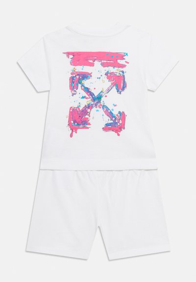 Λευκό δύο κομματιών σετ με κοντά μανίκια και σορτς, με μεγάλο ροζ και μπλε αφηρημένο σχέδιο με σταυρωτά βέλη στην πίσω πλευρά του τοπ.