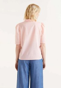 Top de manga abullonada rosa, hecho de tejido ligero, con un corte holgado y un dobladillo redondeado, acompañado de pantalones de mezclilla amplios en azul.