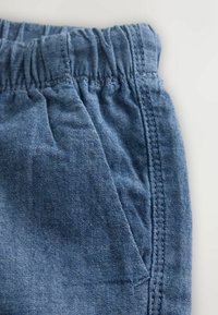 Denimipüksid, millel on elastne vöökoht, helesinine värv, tekstuuriga kangas ja küljetasku nähtava õmbluse detailiga.