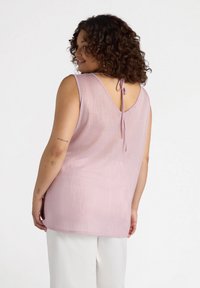 Light pink sleeveless top with a textured finish, a V-back, and adjustable tie detail at the neckline. Flowy design with a relaxed fit.