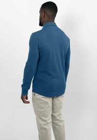 Lange mouwen polo shirt in een effen blauwe kleur, gemaakt van een zachte stof, met een geribbelde kraag en manchetten, gecombineerd met lichtbeige broek.