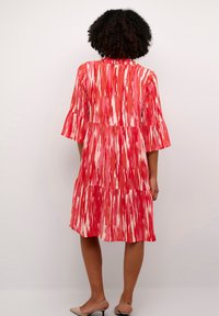 Robe à motifs rouges avec un design à niveaux et des manches évasées. Tissu lisse présentant des bandes abstraites dans des nuances de rouge et de rose.