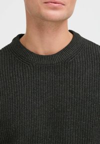 Suéter de punto gris oscuro con una textura acanalada, que presenta un cuello redondo. La tela parece suave y gruesa, adecuada para el clima más fresco.