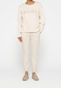 Sweatshirt beige clair avec "10 DAYS" imprimé sur le devant, accompagné de pantalons clairs à rayures et de chaussures beige à enfiler.