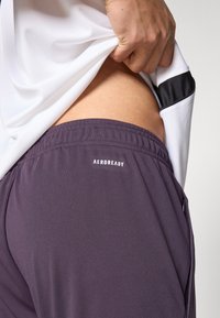 Pantalones cortos deportivos Aeroready en color púrpura oscuro, con cintura elástica, textura suave y un bolsillo lateral con un detalle sutil de la marca.