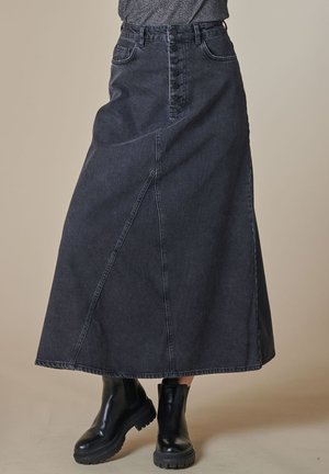 Dark denim maxi skirt featuring a high waist, button-front closure, and angled seams. Paired with black ankle boots.