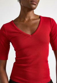 Červené žebrované bavlněné tričko s výstřihem do V a krátkými rukávy, přiléhavý střih a hladká textura.