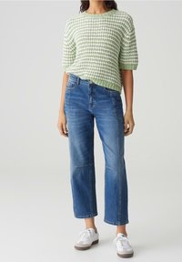Gebreide trui in lichtgroen en witte strepen met korte mouwen, gecombineerd met blauwe wijde jeans en witte sneakers.