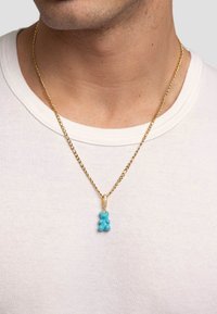 Guld kæde med en blå gelebjørn pendant, med glat tekstur og runde detaljer, sat op på en simpel hvid t-shirt baggrund.