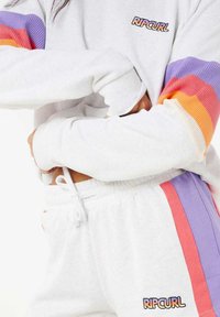 Sweatshirt blanc avec le logo "RIP CURL", présentant des manches en bloc de couleurs côtelées en violet, orange et rose. Pantalons de survêtement coordonnés avec cordon de serrage.