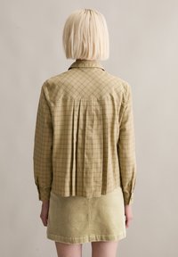 Camicia leggera a quadri beige con righe verdi, con schiena plissettata e maniche lunghe. Abbinata a una gonna in velluto a coste verde dalla trama strutturata.