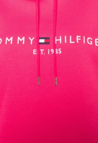 Różowa bawełniana bluza z kapturem z logo w niebieskie, białe i czerwone akcenty, sznurkami zakończonymi metalowymi końcówkami oraz napisem "E.T. 1985".