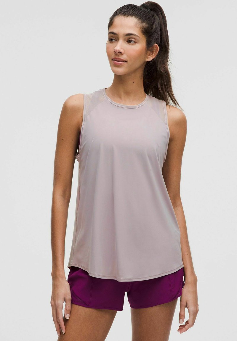 Débardeur de sport gris clair avec une texture lisse, col arrondi et accents transparents aux épaules, associé à un short violet foncé.