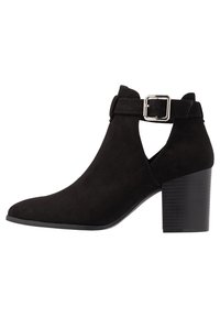 Svart mocka ankelboot med spetsig tå, blockklack och silverfärgad spännsdetalj runt ankeln.