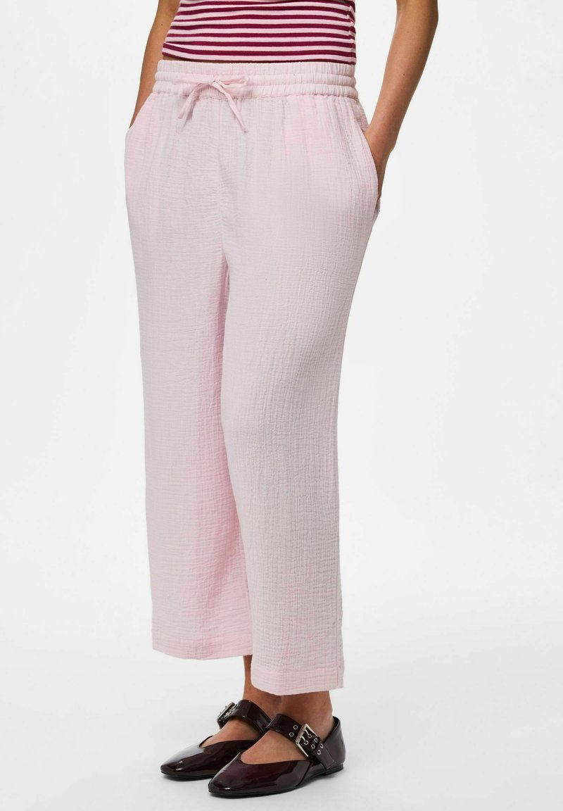 Pantalon large texturé rose clair avec taille élastique à cordon, porté avec des ballerines noires à boucle et un top rayé rouge.