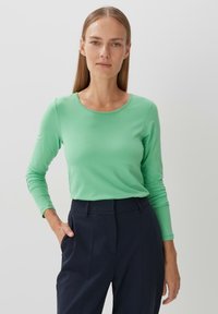 Lange mouwen, top met ronde hals in helder groen. Gemaakt van gladde, lichte stof. Gecombineerd met marineblauwe, tailored broek. Eenvoudig ontwerp.