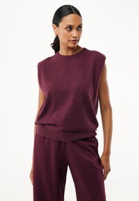 Jersey sin mangas burdeos con un escote redondo y dobladillo acanalado; textura suave con un sutil patrón de puntos y corte relajado. Combinado con pantalones a juego.