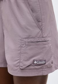 Ανοιχτό μωβ σορτς με πλαϊνή τσέπη που διαθέτει ένα μικρό φερμουάρ και επιγραφή με το λογότυπο της Columbia Sportswear Company.