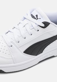 Weiße Leder-Sneaker mit schwarzen Akzenten, ausgestattet mit einer strukturierten Seitenansicht, Perforationen und flachen Schnürsenkeln. Puma-Logo auf der Zunge.